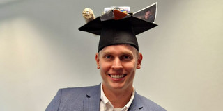 Zu sehen ist Nils Jahn mit einem Doktorhut nach seiner erfolgreichen Promotionsprüfung